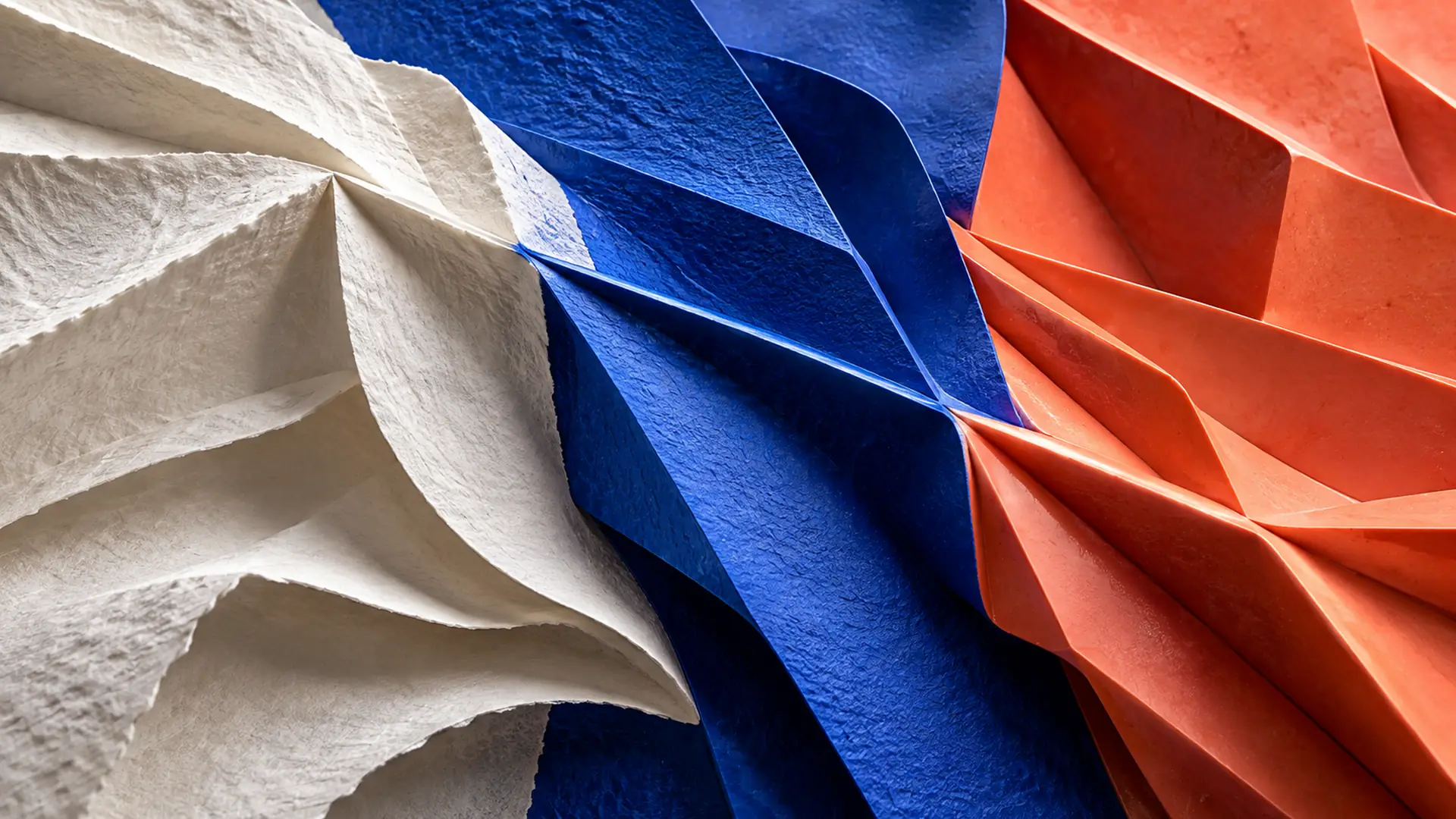 A continuous sculptural fold evolving from white paper through blue and coral surfaces